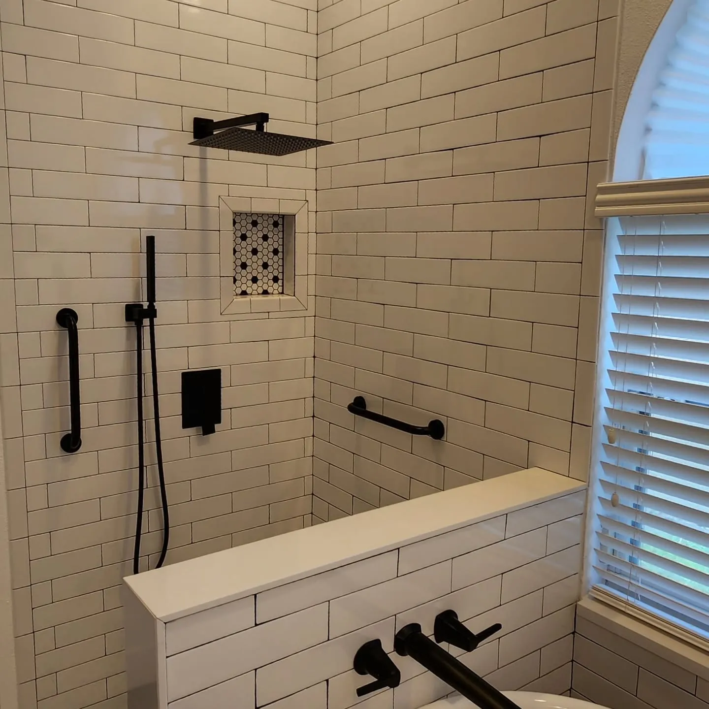 Subway tile shower with matte black fixtures and arched window